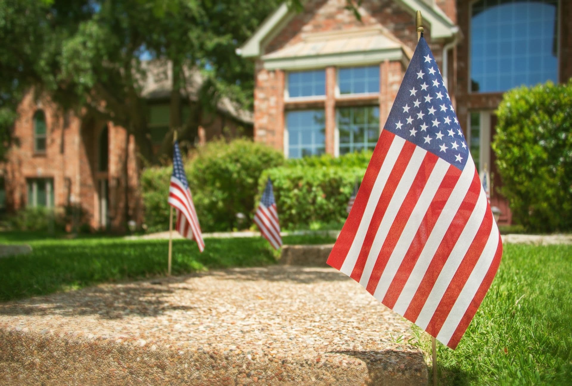 American flags line a walkway in front of a brick house.