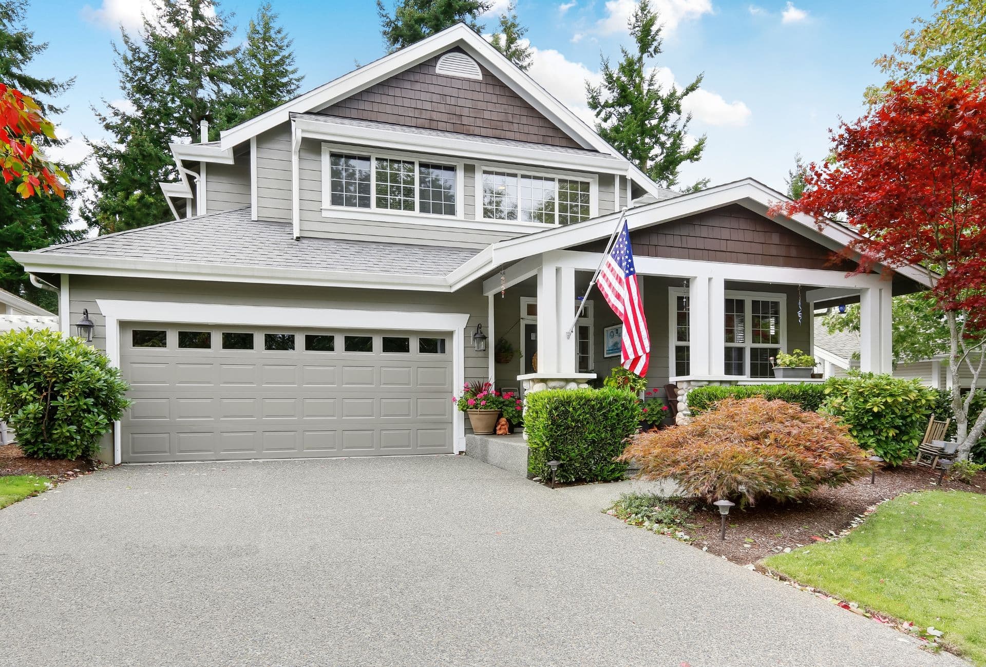A grey house with garage and driveway, and column porch with an American flag.